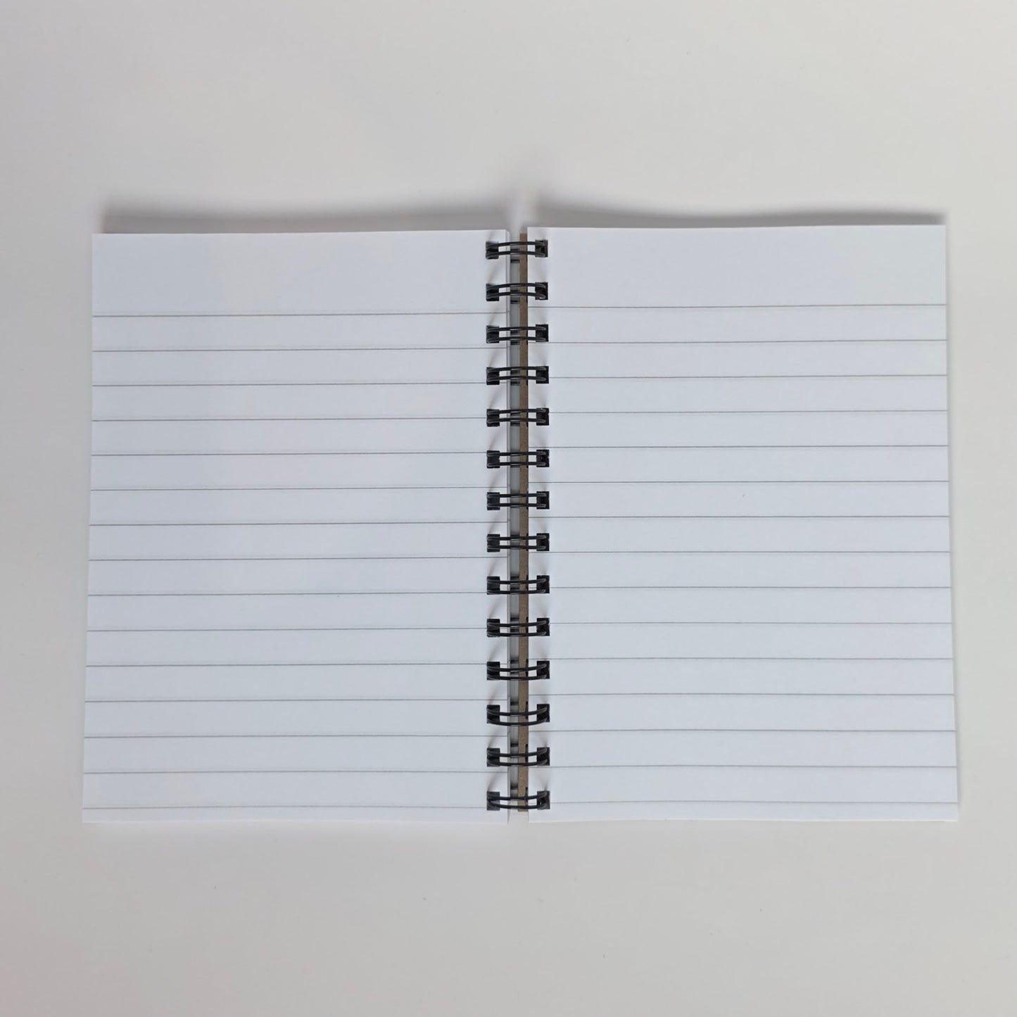White-lined pages inside a spiral-bound 5x7 notebook with silver wire and smooth paper