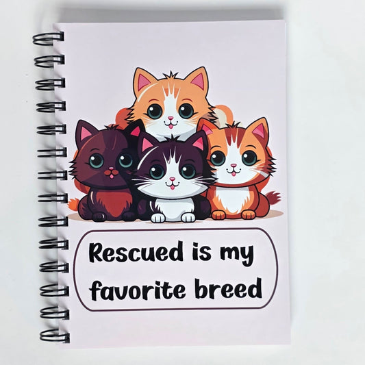 Cute cat-themed notebook with cartoon rescue cats and the phrase “Rescued is my favorite breed” on a light pink cover