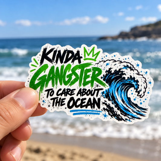 Hand holding a Kinda Gangster to Care About the Ocean sticker in front of the sea.