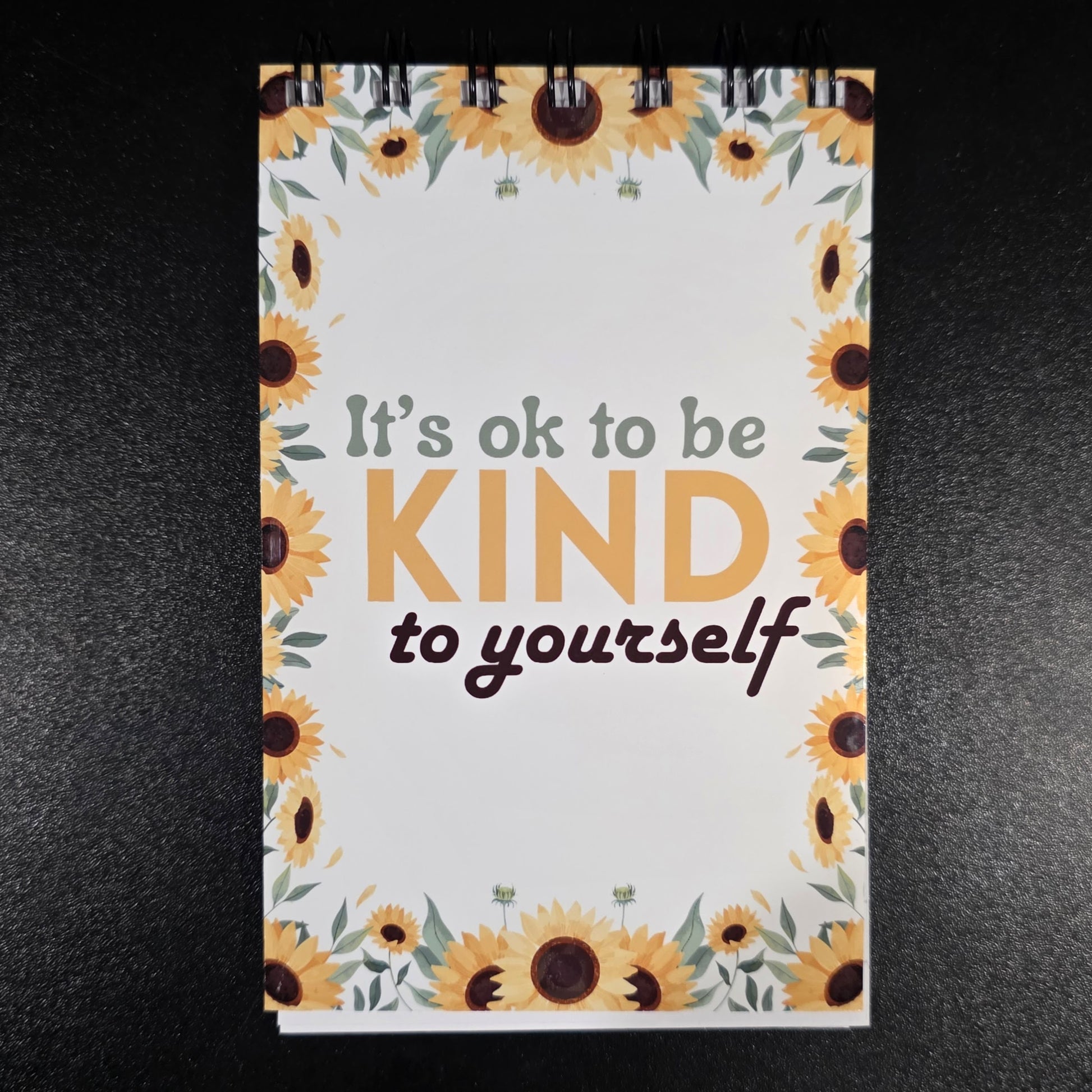 Notebook with sunflower design and motivational quote on a dark background